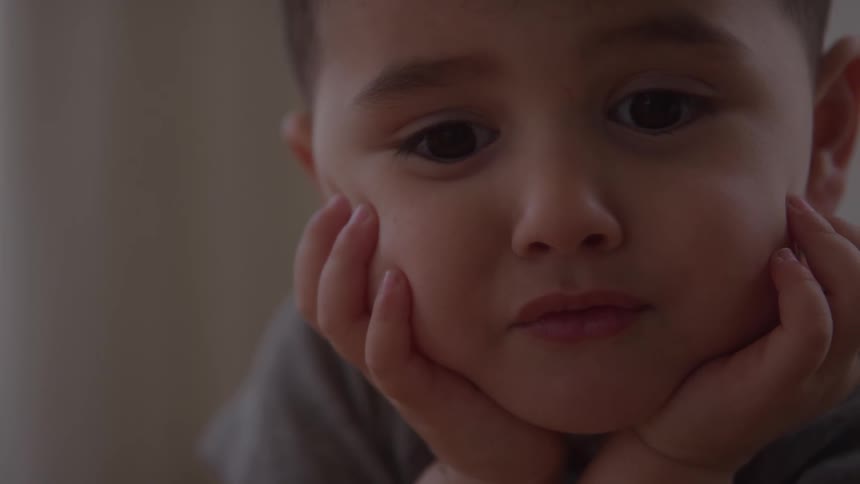 Young boy sits with his chin cupped in his own hands