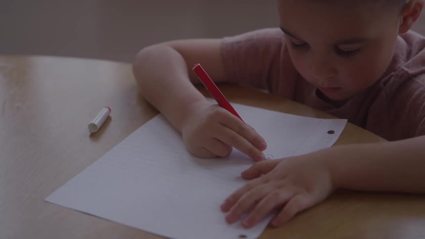 Young boy sitting at the table drawing on paper