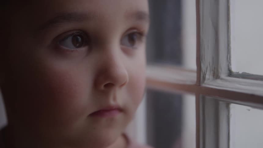 A young boy continuously looks out of the window of his room