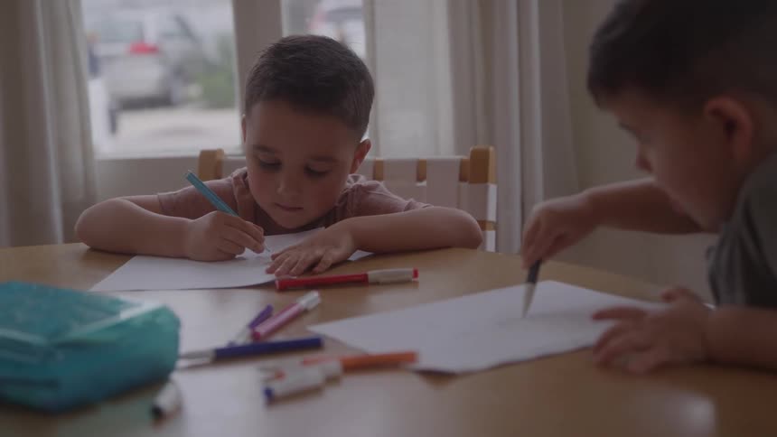 Two young boys sitting at the table drawing on paper