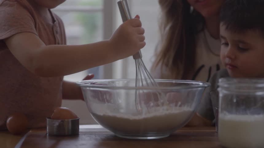A mother and her children mix ingredients in a large bowl while baking together at home