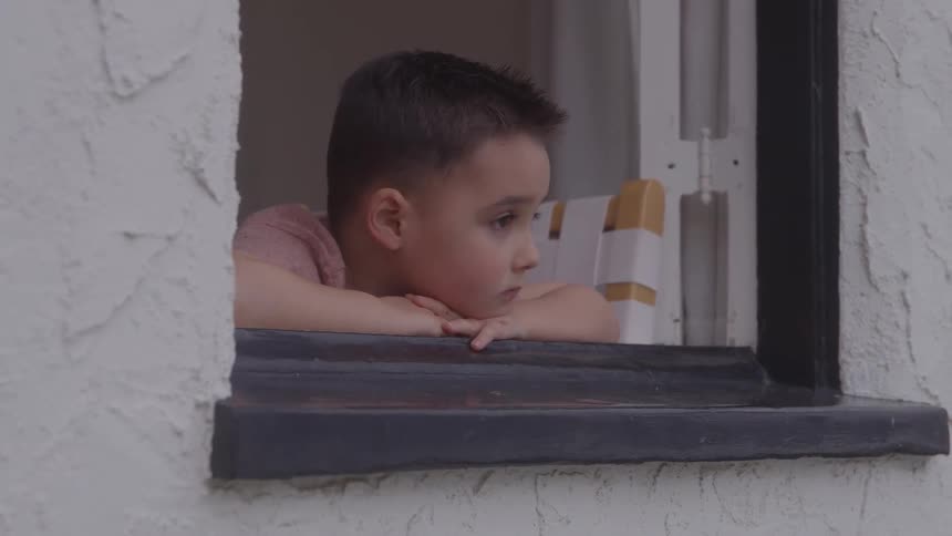 Young boy sits in a chair while leaning on the windowsill and looking outside