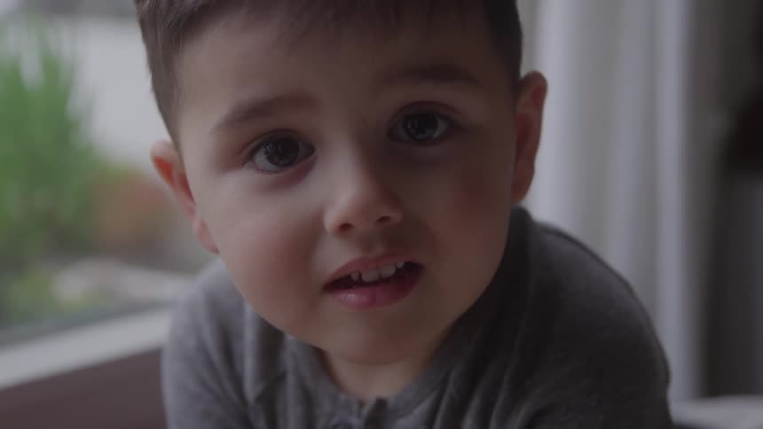 Closeup of a young boy looking curiously into the camera indoors