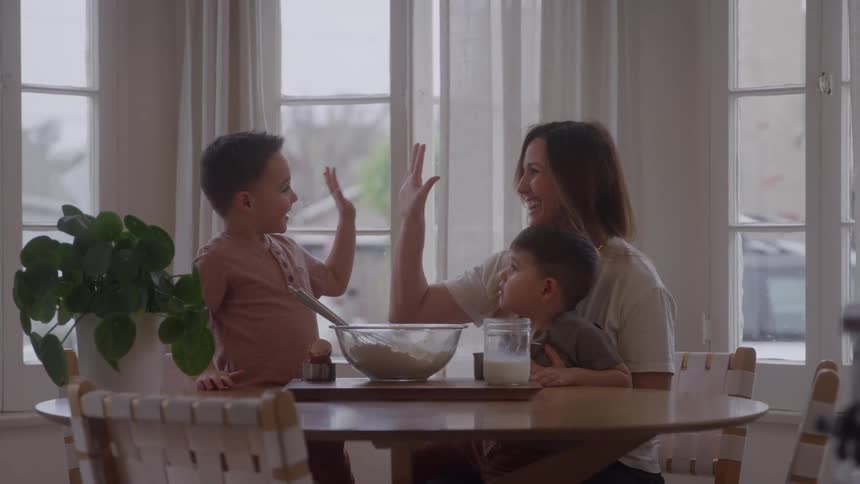 Mother and son exchange a high five while a younger boy sits in her lap