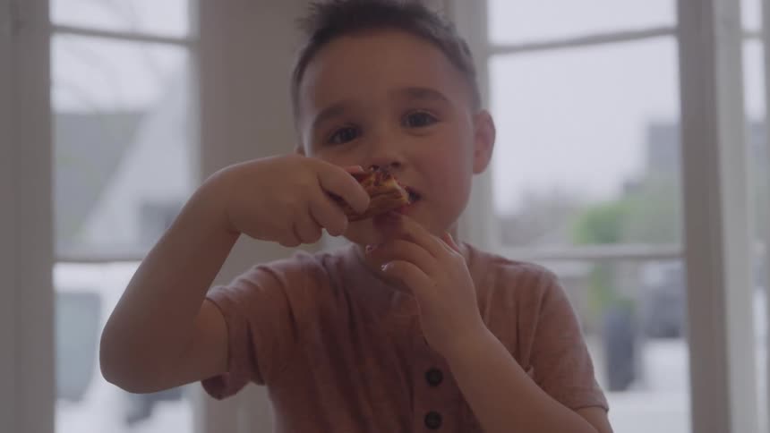 The video is a tight closeup of a young boy in a pink shirt brushing his teeth he is standing in front of a window and has a focused intent expression on his face