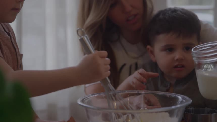 A mother and two children bake together in a bright home kitchen