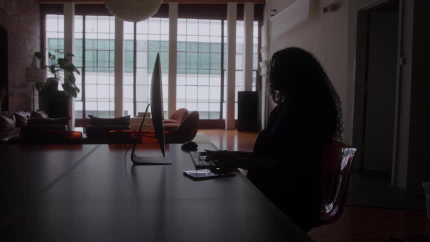A woman works on her computer in a dimly lit modern office