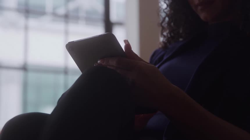 A woman is sitting down typing on a tablet