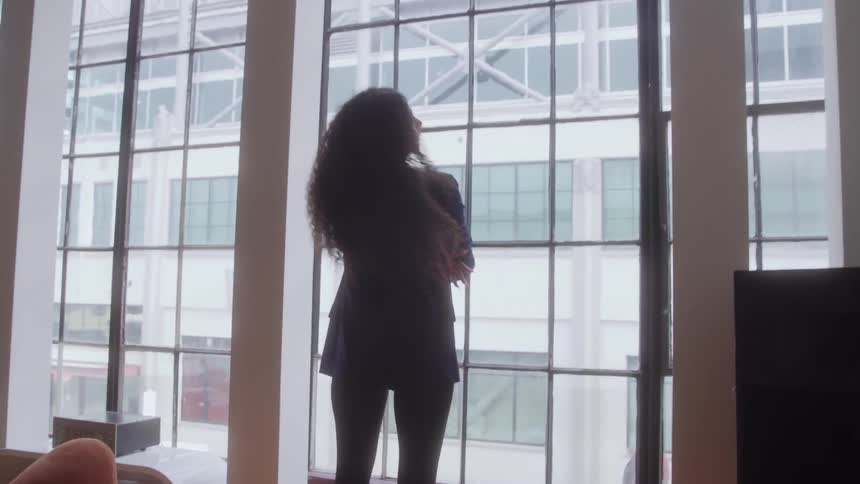 A woman stands by large windows looking outside in a modern office