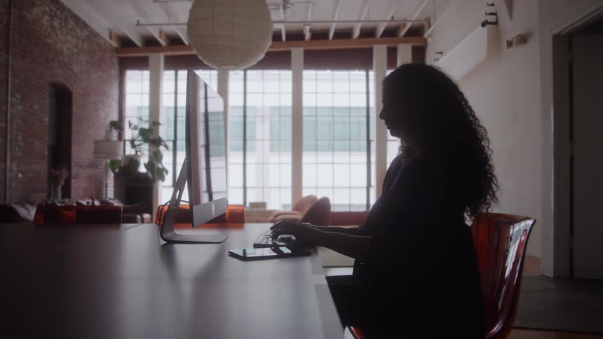 Person typing on computer in modern space with large windows and industrial decor