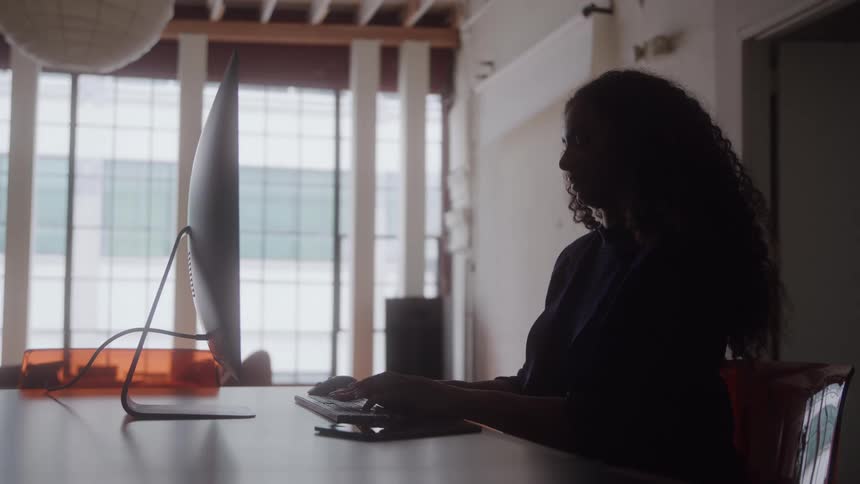 A woman in an office typing on a computer keyboard