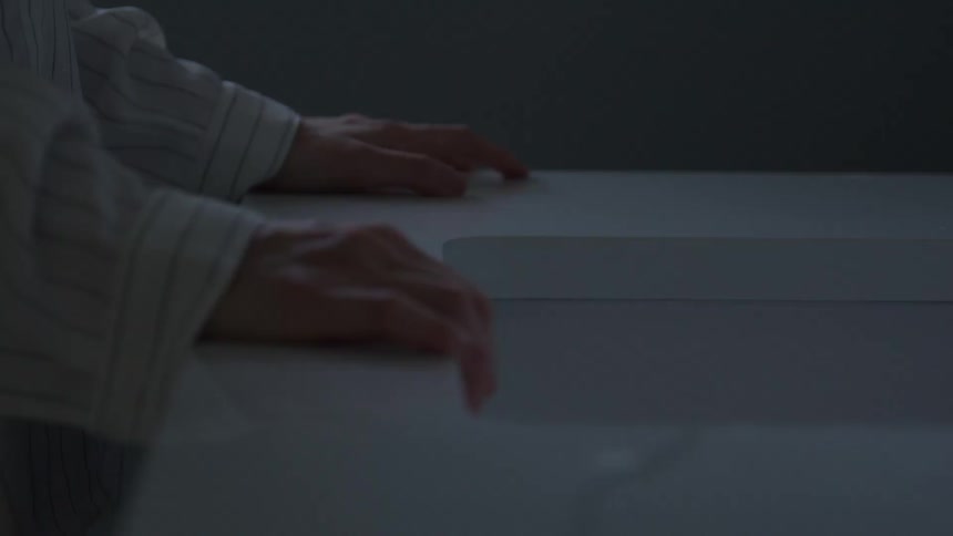 Hands resting on white surface in softly lit setting with striped clothing