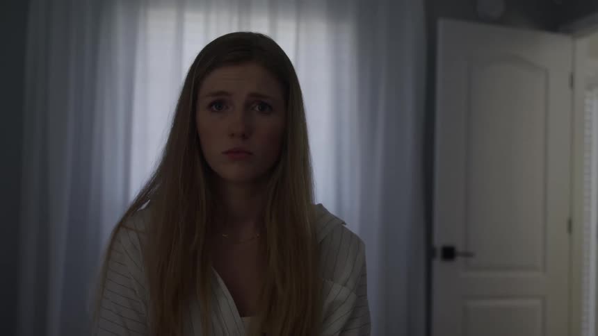 Woman stares with a serious expression in a softly lit setting