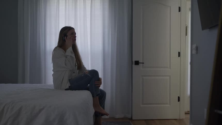 Woman sits on the edge of the bed talking on the phone in a bright room