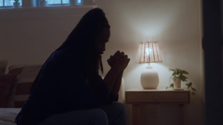 A stressed man sits on a bed in a dimly lit bedroom