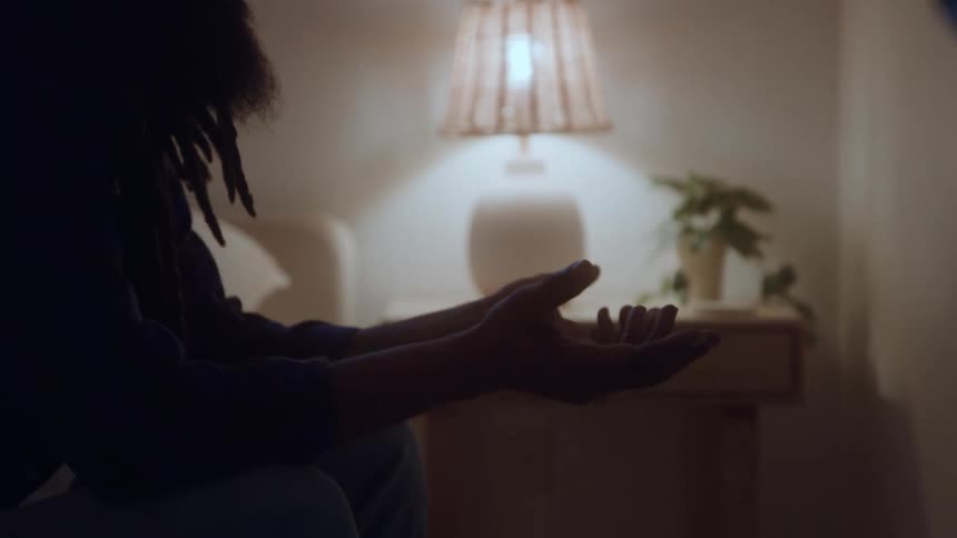 Man sits in silence looking at his hands before a lit lamp