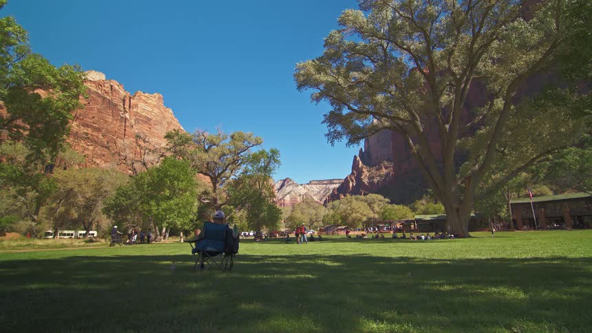 Couple sits on chairs enjoying a park surrounded by cliffs under a blue sky