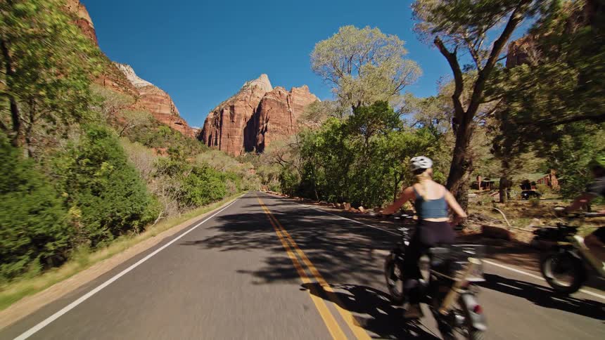 Group of cyclists rides along a road surrounded by trees and mountains under a blue sky