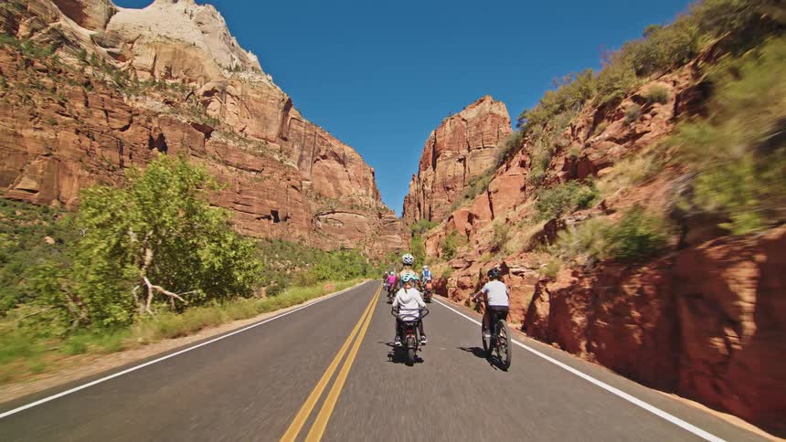 A family and other cyclists ride their bikes down a scenic road through a sunny majestic red rock canyon