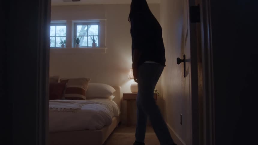 Man sitting on the edge of the bed reflects silently in a room lit by a lamp