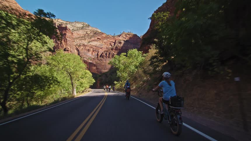 Cyclists riding along a road surrounded by rocks and greenery under a blue sky