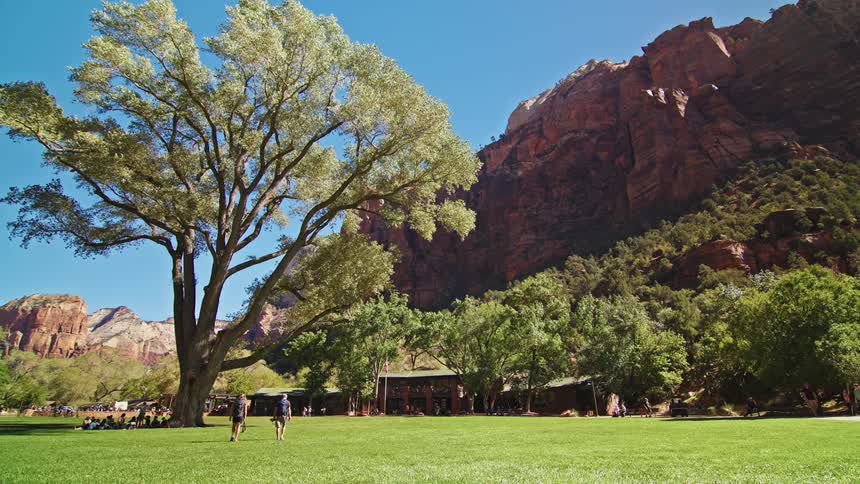 Man walks across a wide lawn surrounded by trees and rocky mountains