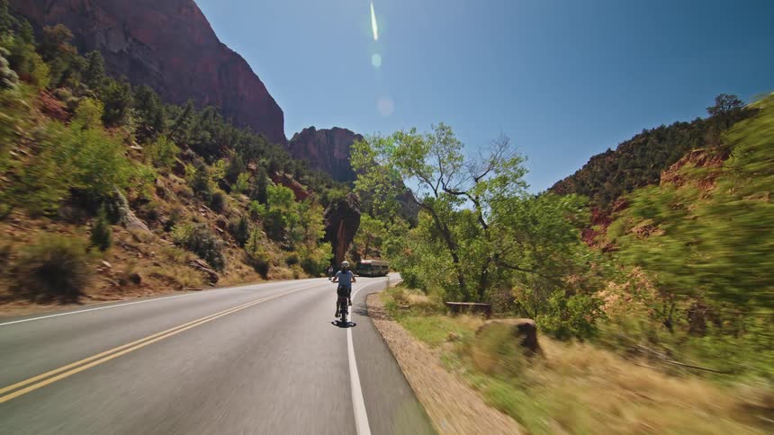 Cyclists ride along a winding road between mountains under a sunny sky