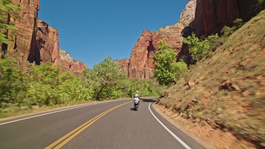 Cyclists ride along a road between canyons under a blue sky