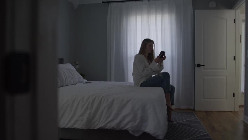 A thoughtful woman sitting on her bed by a window where she answers a phone call