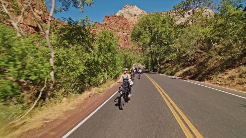 Woman rides a bike with a child on a road surrounded by trees and mountains