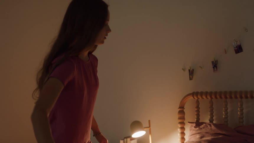 A young woman makes her bed preparing for a nights rest with a lamp beside the bed