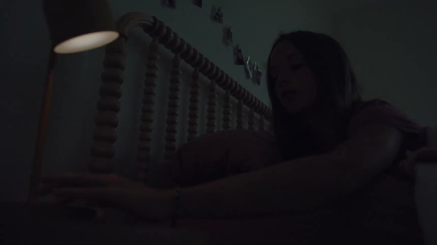Girl lying down reaching out her hand and turning off the bedside lamp