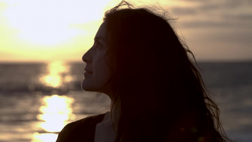 Woman looks at the sea at sunset with her face lit by golden light