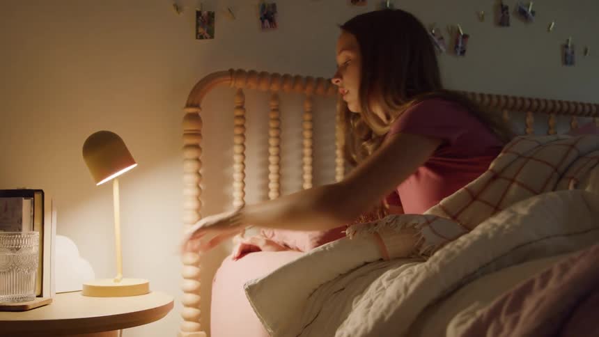 Girl turns off the bedside lamp and lies down on the bed