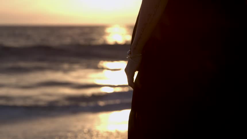 A person stands silhouetted on a beach as the sun sets casting warm golden reflections on the water