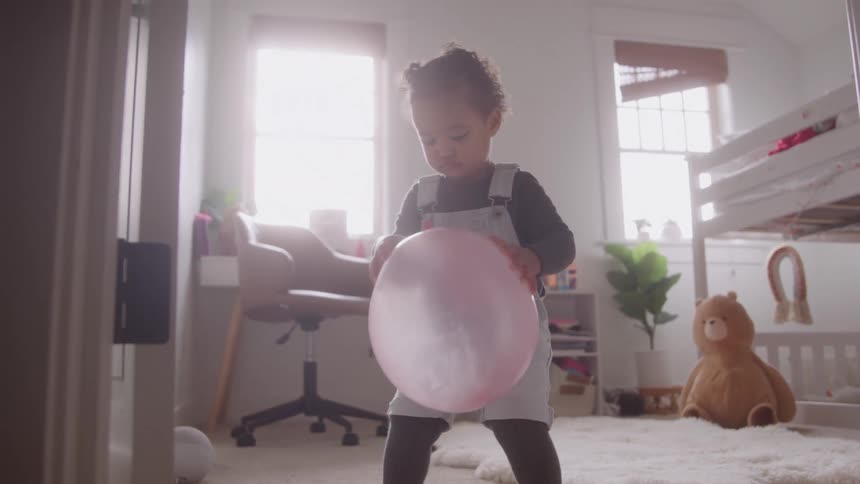 A small girl picks up a pink balloon while in her bedroom