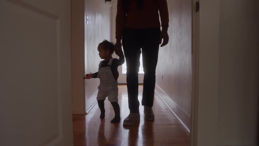 The video is a lowangle backlit shot of a man and a small child walking down a long narrow hallway with hardwood floorsthe figures are mostly silhouetted against the bright light coming from the closed glass door at the end of the hall as they w