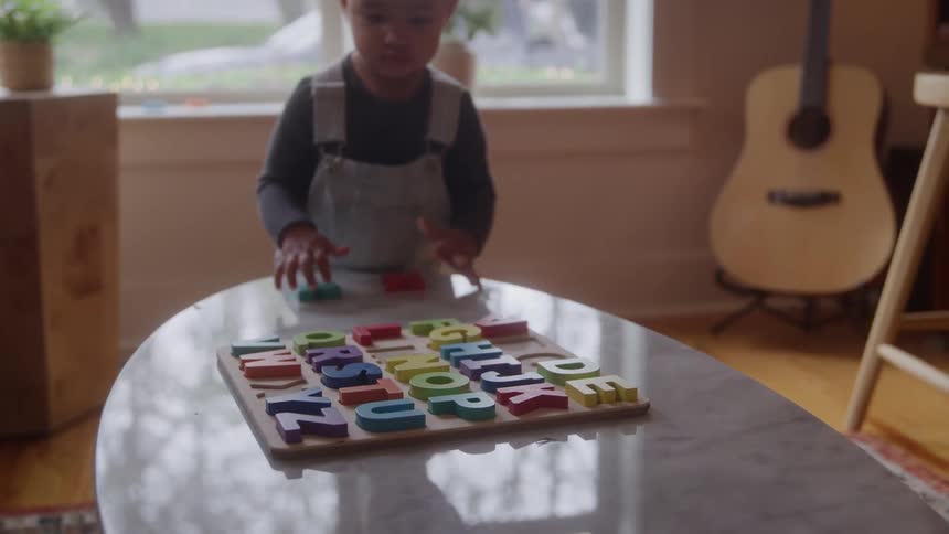 A toddler plays with colorful alphabet puzzle pieces on a table in a cozy sunlit room