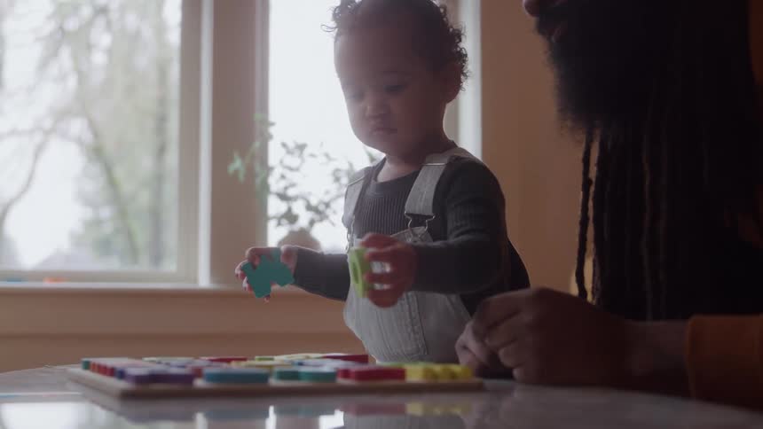 Father and daughter play with colorful pieces on the table near the window