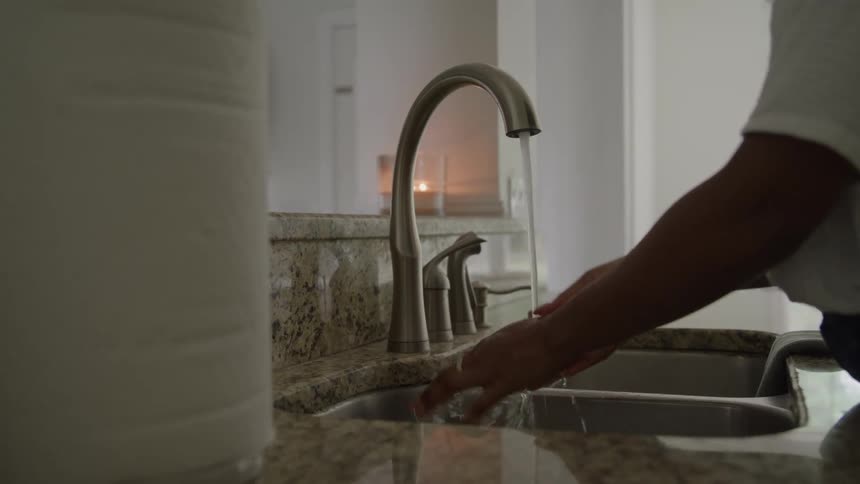 A person washes their hands under running water in a bright kitchen