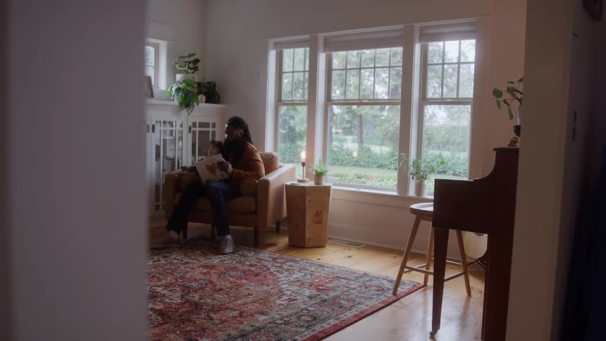 A father reads a book to his son while sitting together in a sunlit living room