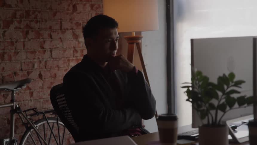 A young asian man working with a desktop computer while sitting at a desk in an office during daytime