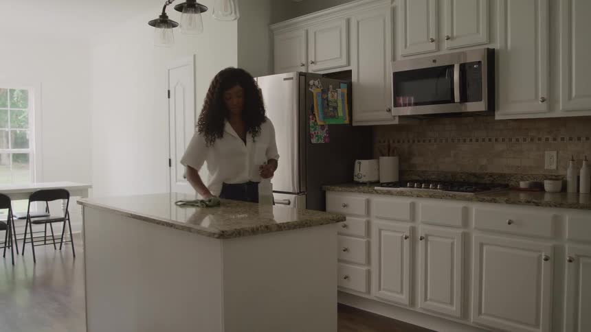 A woman wipes the kitchen counter in a bright modern home