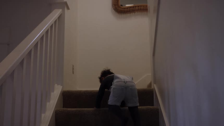 Child climbs the stairs on hands and knees in a welllit home