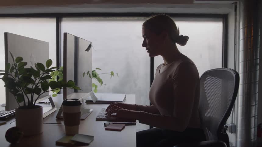 The woman talks in the office and types on her keyboard