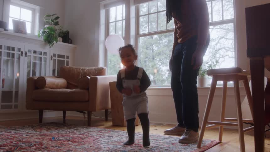 Child plays with a balloon while an adult watches smiling in the bright living room
