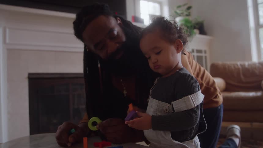 Young bearded black man and female biracial toddler playing on a coffee table on a living room indoors during day time