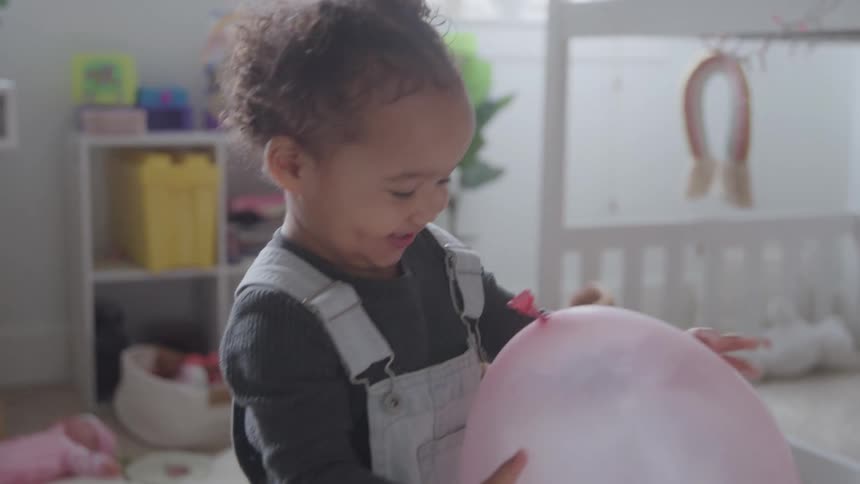 Child holds a pink balloon while playing in a bright room