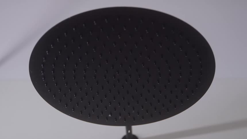 A close view shows a large black circular rainfall showerhead with many small nozzles positioned against a white bathroom ceiling