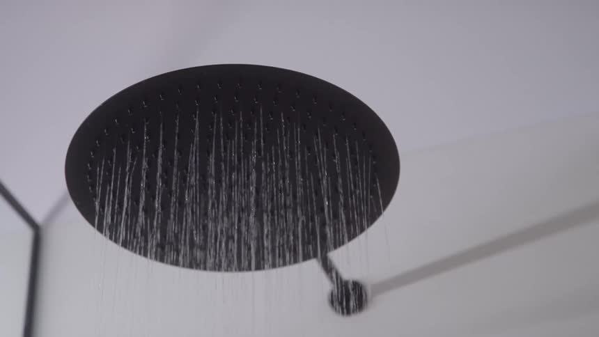 Modern black showerhead releasing streams of water in a bright bathroom